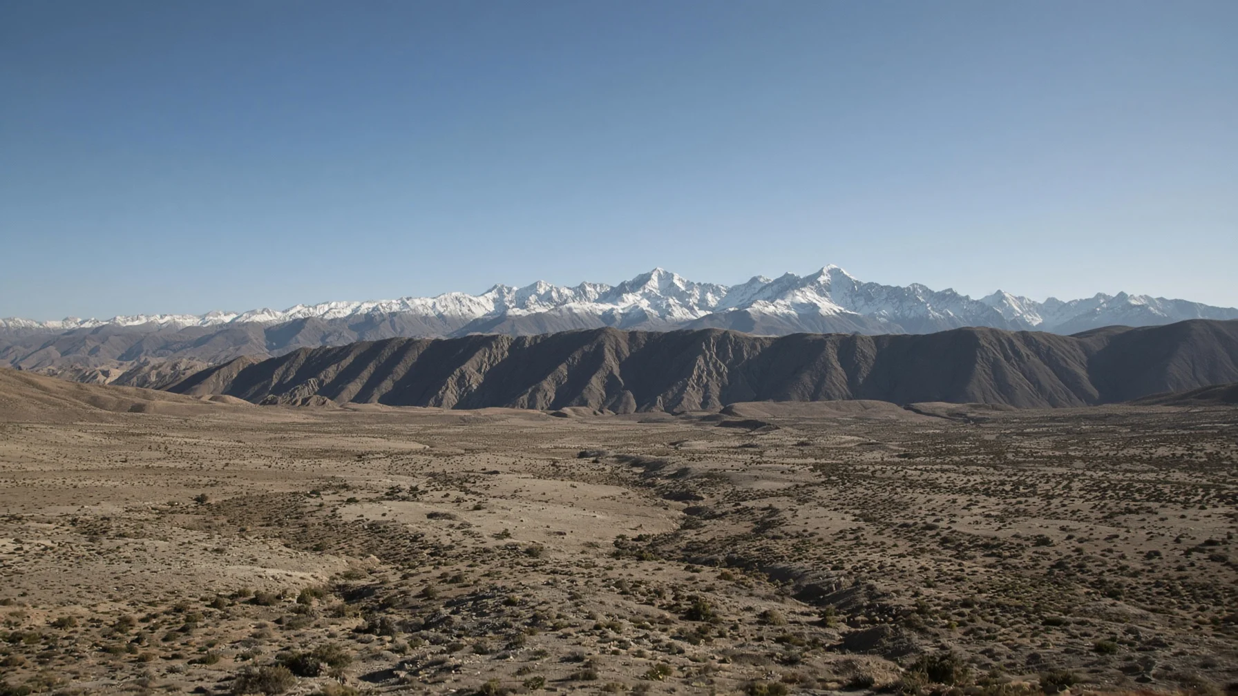 A rain-shadow landscape of dry valleys and sparse vegetation stretching beyond a high mountain range