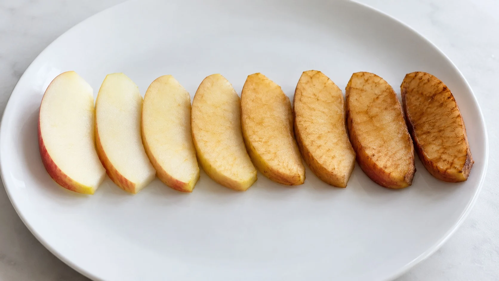 Apple slices on a white plate changing in sequence from a white cut face on the left to a deep brown one on the right