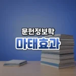 마태효과 썸네일: 밝은 나무 책상 아래쪽에 학술지와 논문이 높이 쌓인 더미와 얇은 더미가 나란히 놓이고, 뒤로 부드러운 남색 빛이 번지며 가운데·위쪽에 글자를 올릴 여백이 있는 모습