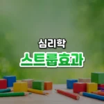 스트룹효과 썸네일: 화면 아래쪽 밝은 책상 위에 알록달록한 나무 블록과 색연필이 흩어져 있고, 부드러운 초록빛이 위로 번져 가운데·위쪽에 글자를 올릴 여백이 있는 모습