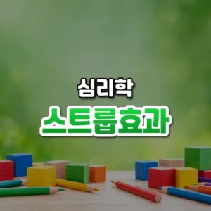 스트룹효과 썸네일: 화면 아래쪽 밝은 책상 위에 알록달록한 나무 블록과 색연필이 흩어져 있고, 부드러운 초록빛이 위로 번져 가운데·위쪽에 글자를 올릴 여백이 있는 모습